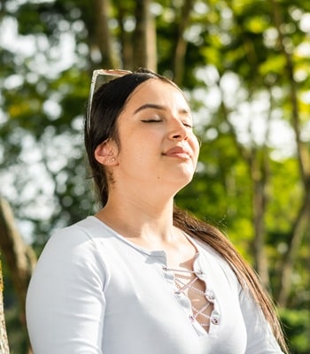 Eine Frau steht im Sommer bei Sonnenschein draußen und genießt das schöne Wetter