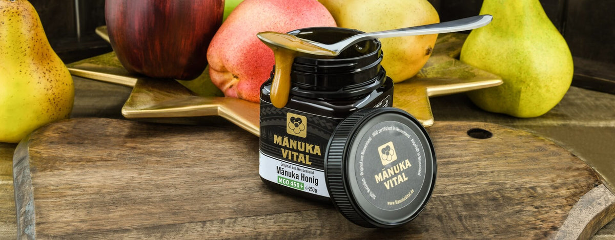 Offener Manuka Vital Honig auf einem Holztisch mit Äpfel und Birnen im Hintergrund